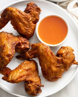 Fried Chinese Chicken Wings on a white plate with sweet and sour sauce on the side.