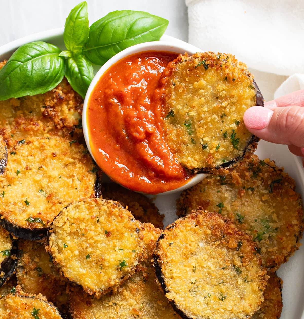 A sliced of fried eggplant being dipped into marinara sauce.