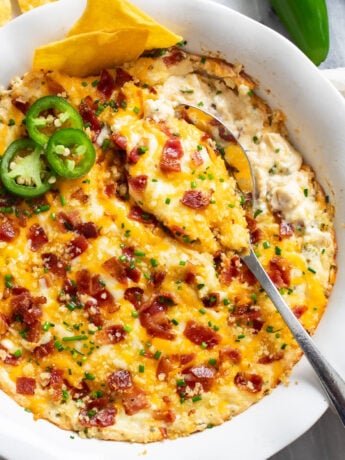 A spoon scooping up Jalapeno Popper Dip from a baking dish.