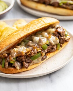 A Philly Cheesesteak Sandwich on a plate with potato chips in the back.