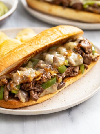 A Philly Cheesesteak Sandwich on a plate with potato chips in the back.