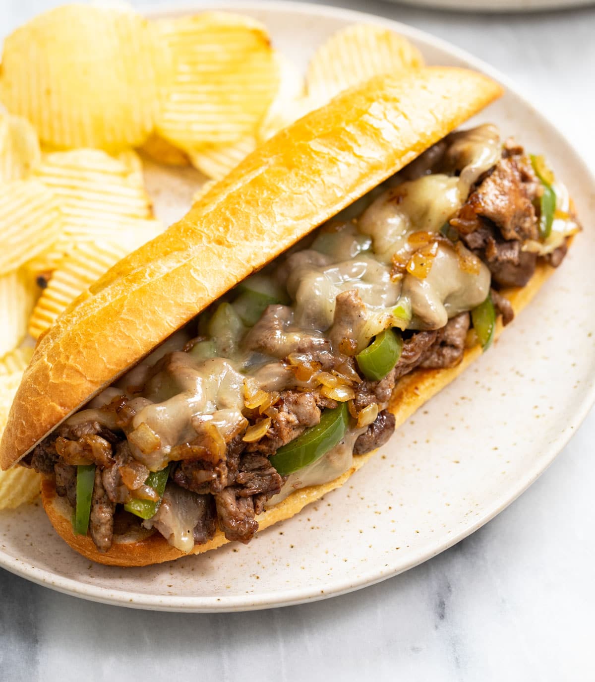 Philly Cheesesteak on a plate with chips in the background
