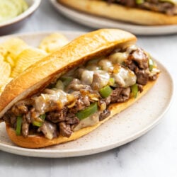 A Philly Cheesesteak Sandwich on a plate with melted cheese and peppers and onions.