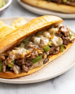 A Philly Cheesesteak Sandwich on a plate with melted cheese and peppers and onions.