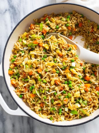 A white skillet with Vegetable Fried Rice and a white spoon on the side.