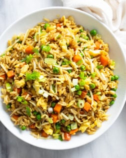 Vegetable Fried Rice in a white bowl with peas, carrots, sprouts, and green onions.