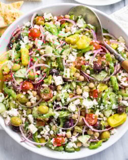 Greek Salad in a white bowl with vegetables, chickpeas, dressing, and feta.