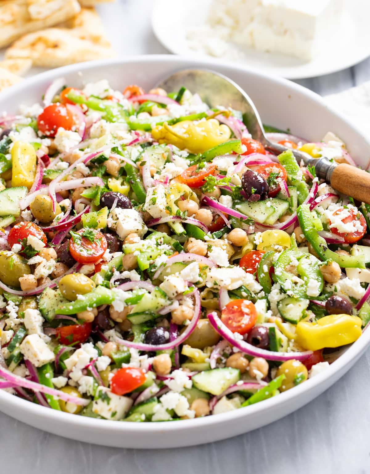 Side view of Greek Salad in a white bowl with vegetables, chickpeas, dressing, and feta.