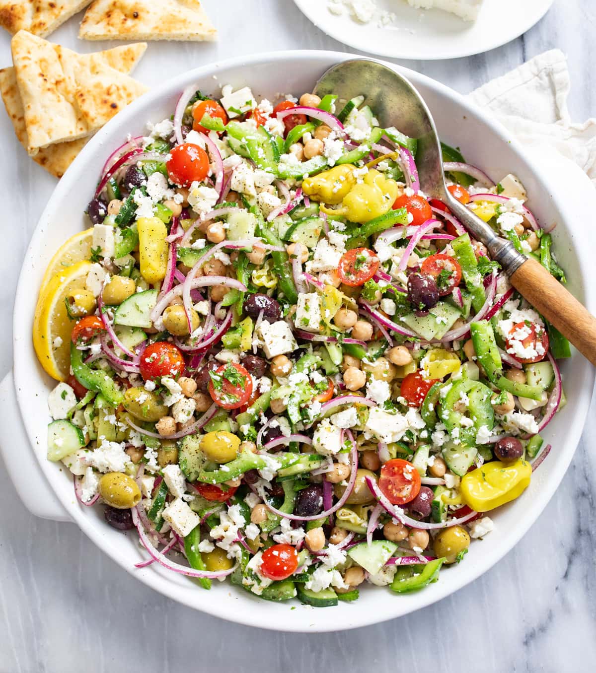 Overhead view of classic Greek Salad with vegetables, feta, chickpeas, and homemade dressing.
