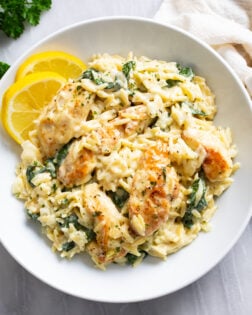 Lemon Chicken Orzo in a creamy sauce with spinach in a white bowl with lemon slices on the side.