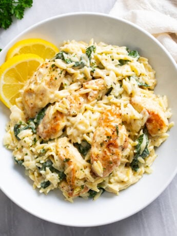Lemon Chicken Orzo in a creamy sauce with spinach in a white bowl with lemon slices on the side.