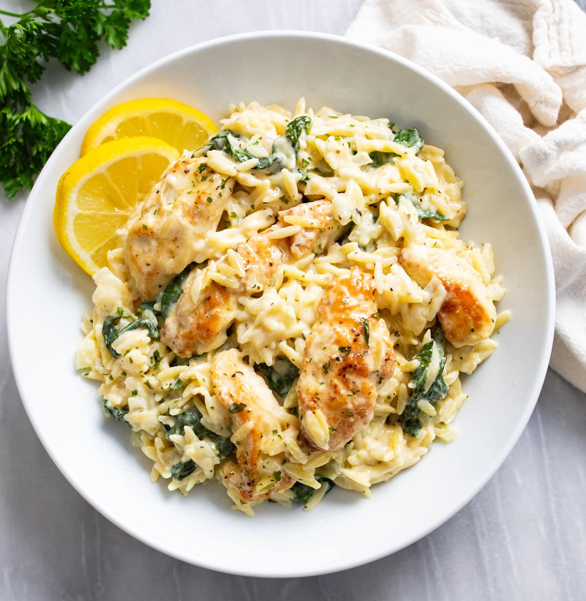 Lemon Chicken Orzo in a creamy sauce with spinach in a white bowl with lemon slices on the side.