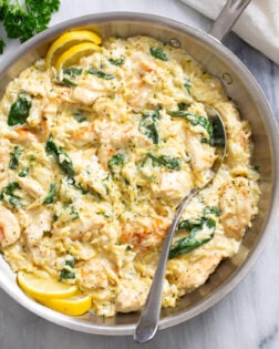 A skillet with Lemon Chicken Orzo in a creamy sauce with spinach and a spoon on the side.