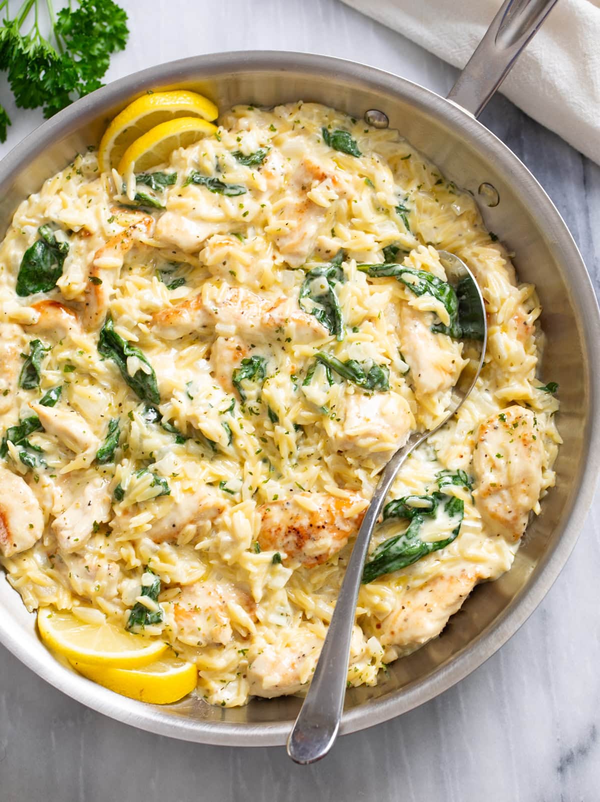 A skillet with Lemon Chicken Orzo in a creamy sauce with spinach and a spoon on the side.