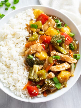 Pork Stir Fry with a brown sauce on a white plate with a bed of white rice.