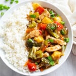 Pork Stir Fry in a brown stir fry sauce with strips of pork, vegetables, and a side of white rice on a plate.