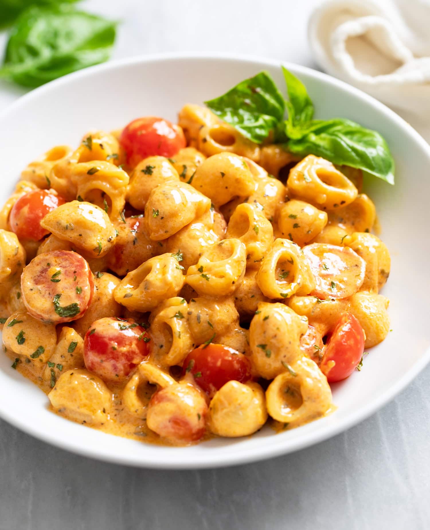 Cherry Tomato Pasta in a white pasta bowl with fresh basil in the background.