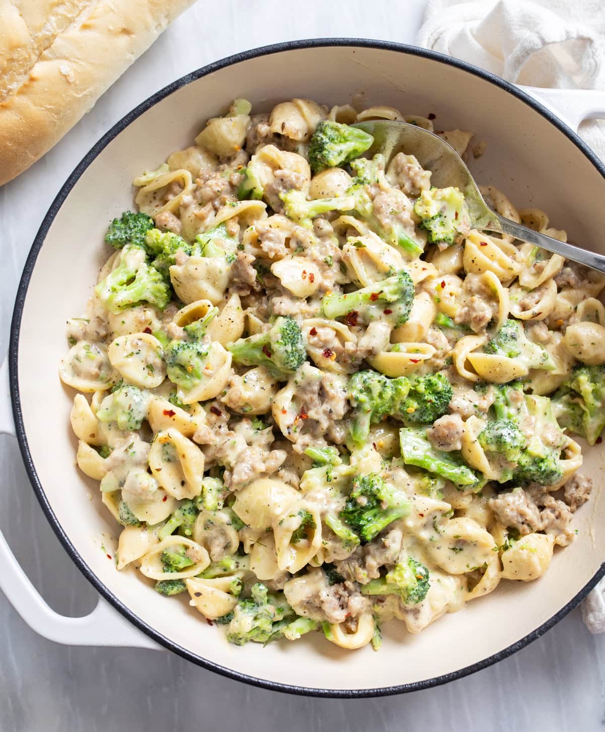 Sausage and Broccoli Pasta in a creamy sauce in a skillet with a spoon on the side.