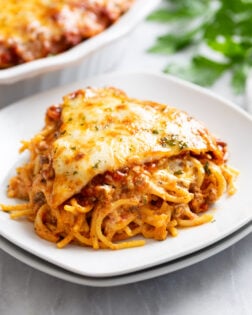 A slice of Spaghetti Pie on a white plate with parsley on top.