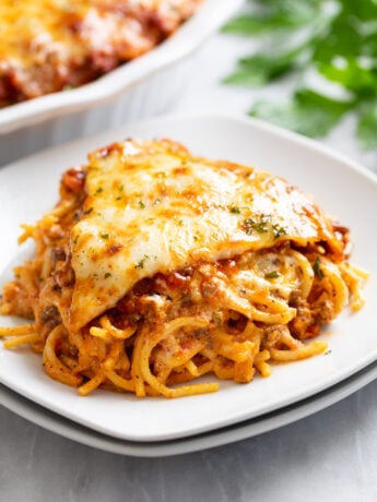 A slice of Spaghetti Pie on a white plate with parsley on top.