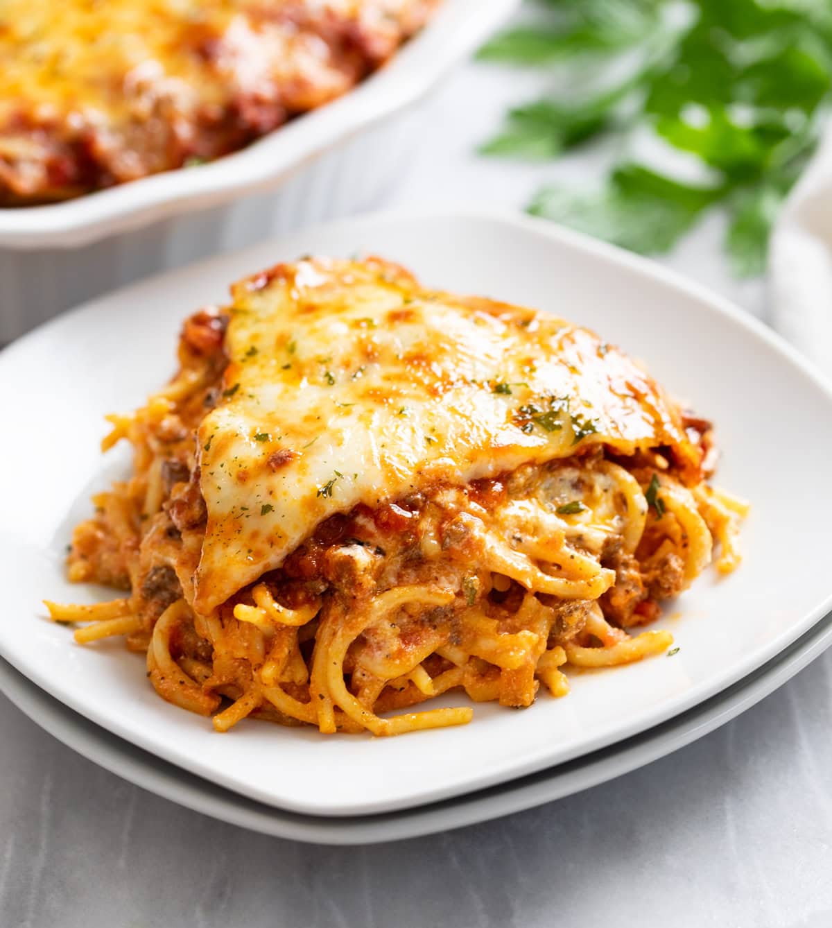 A slice of Spaghetti Pie on a white plate with parsley on top.