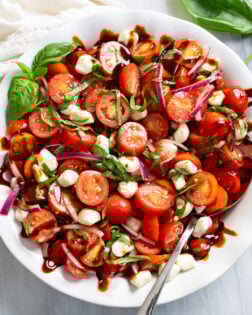 Tomato Salad in a white bowl with fresh basil, mozzarella, red onions, and balsamic glaze.