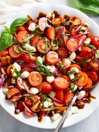 Tomato Salad in a white bowl with fresh basil, mozzarella, red onions, and balsamic glaze.