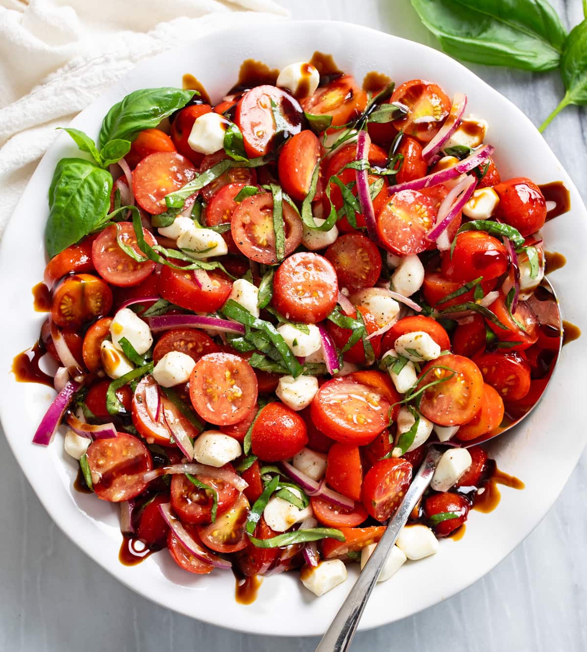 Tomato Salad in a white bowl with fresh basil, mozzarella, red onions, and balsamic glaze.