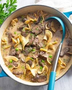 Beef Stroganoff Soup in a blue soup pot with noodles, beef, mushrooms, peas, and a ladle on the side.