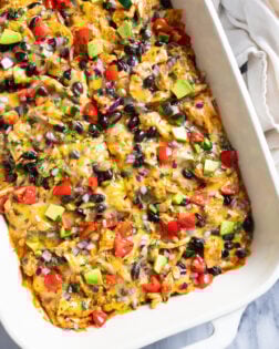 Chicken Enchilada Casserole in a white casserole dish with assorted colorful toppings on top.