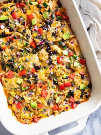 Chicken Enchilada Casserole in a white casserole dish with assorted colorful toppings on top.
