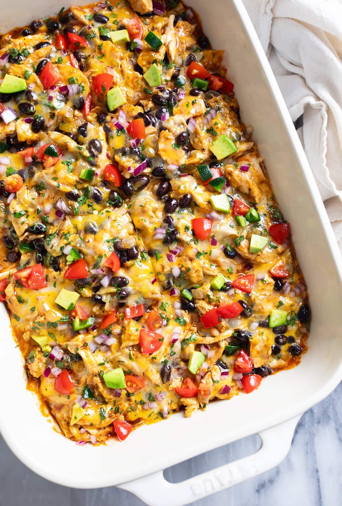 Chicken Enchilada Casserole in a white casserole dish with assorted colorful toppings on top.