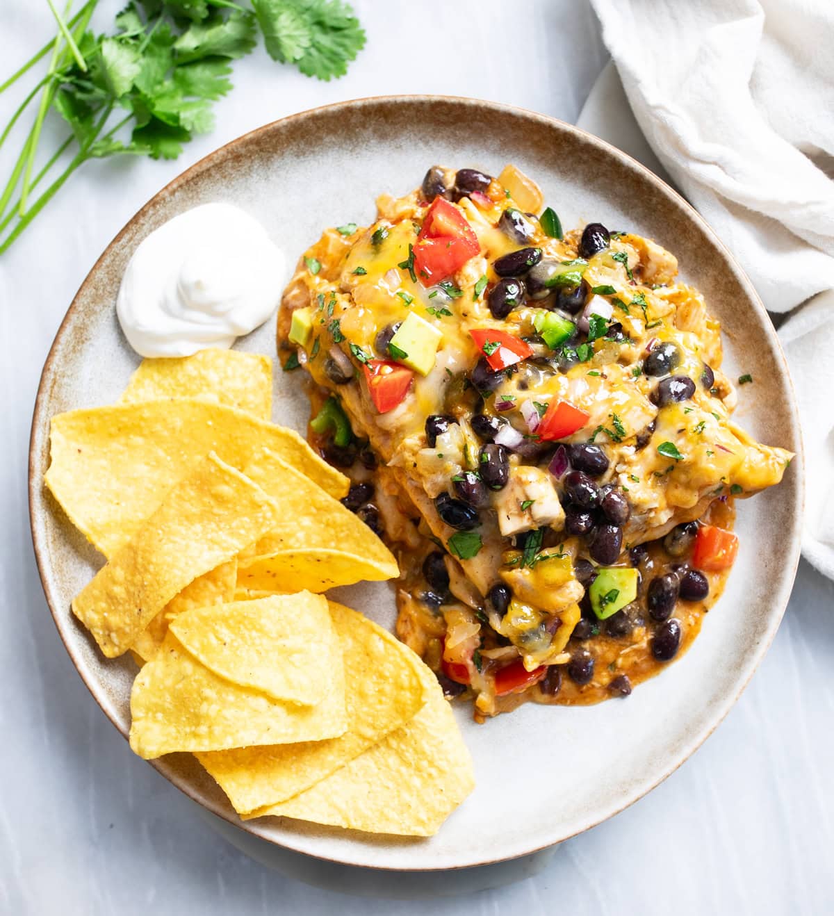 Chicken Enchilada Casserole on a plate with a side of sour cream and tortilla chips.
