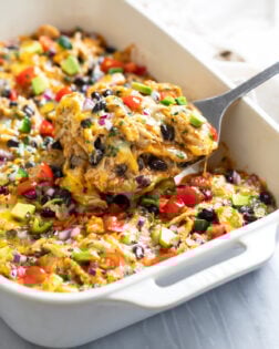 Side view of a spatula lifting out a slice of Chicken Enchilada Casserole from a white baking dish.