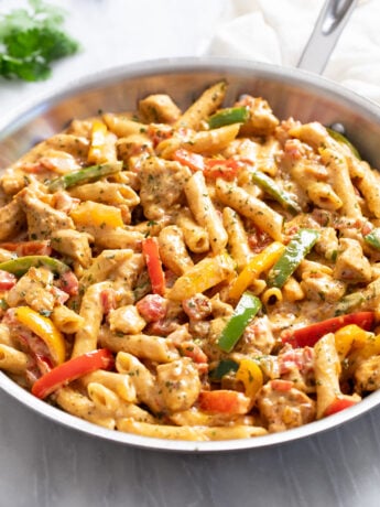 A skillet of Chicken Fajita Pasta with penne, bell peppers, chicken, and a cream sauce.
