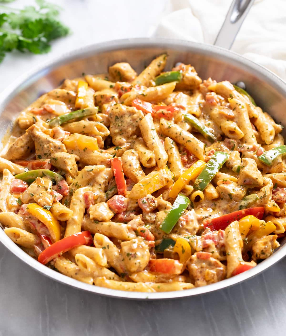 A skillet of Chicken Fajita Pasta with penne, bell peppers, chicken, and a cream sauce.