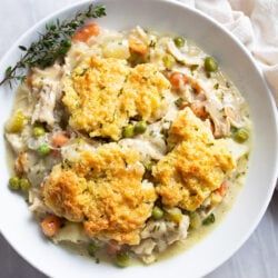A white bowl filled with Chicken Pot Pie Casserole with fresh thyme on the side.