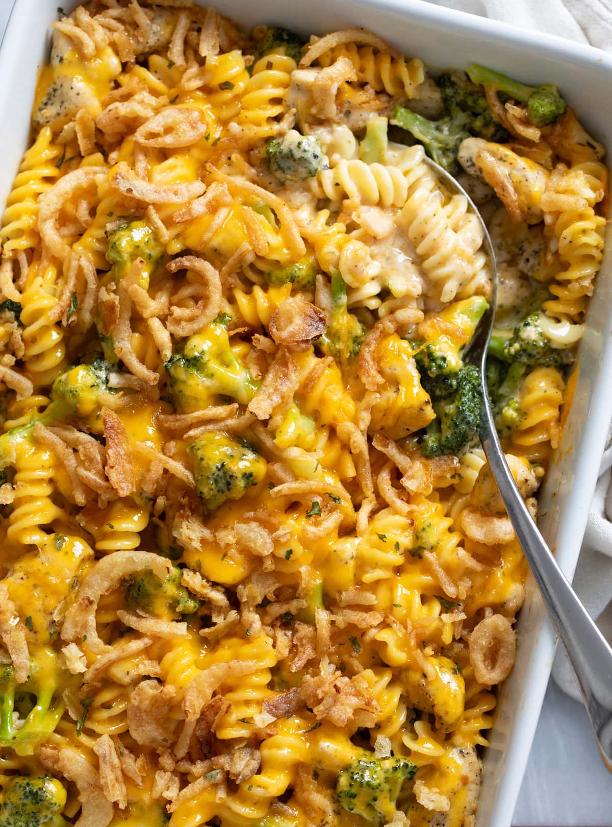 A Chicken and Broccoli Pasta Bake in a casserole dish with a spoon on the side.