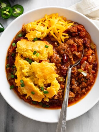 Chili Corn Casserole in a white bowl with a spoon on the side and cheese on top.