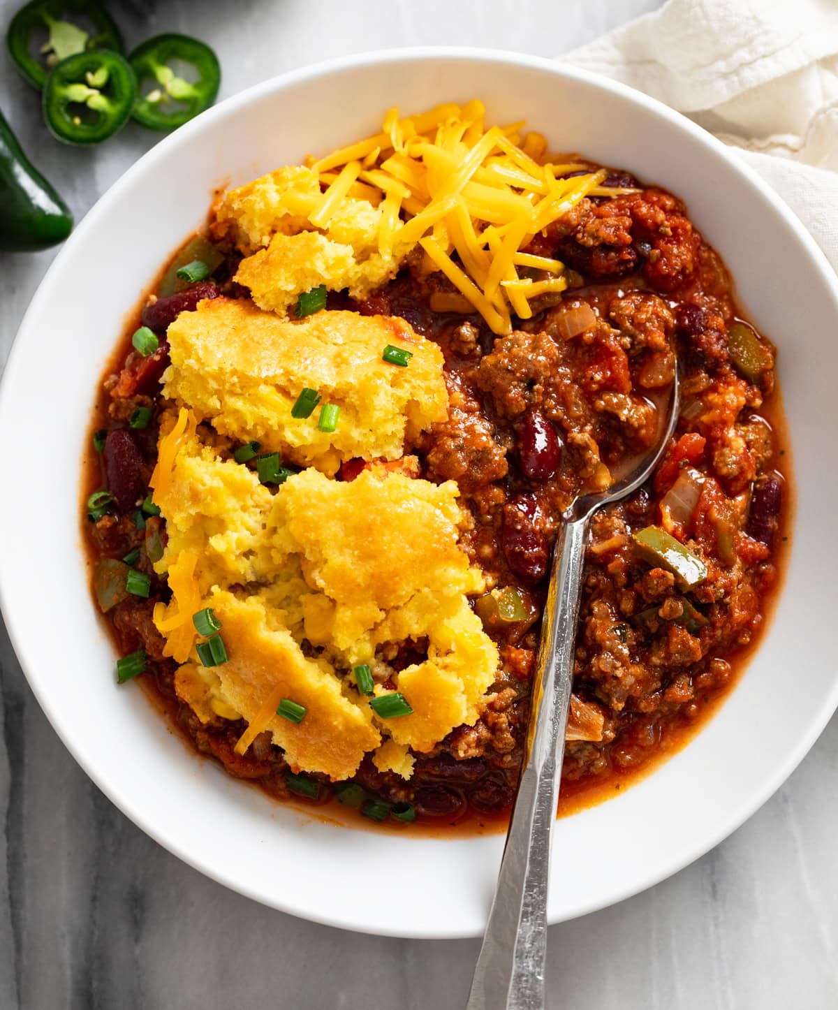 Chili Corn Casserole in a white bowl with a spoon on the side and cheese on top.