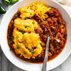 Chili Cornbread Casserole in a white bowl with a spoon on the side and shredded cheese on top.