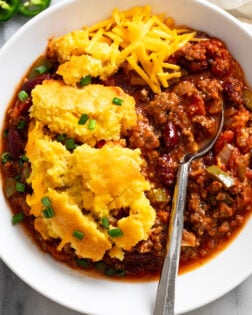 Chili Cornbread Casserole in a white bowl with a spoon on the side and shredded cheese on top.