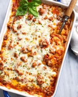 Ravioli Lasagna in a casserole dish with a serving spoon on the side and fresh basil on the side.