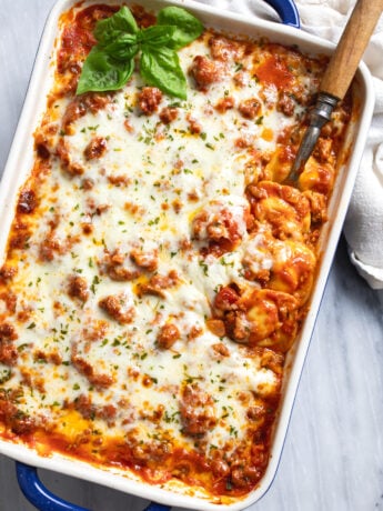 Ravioli Lasagna in a casserole dish with a serving spoon on the side and fresh basil on the side.