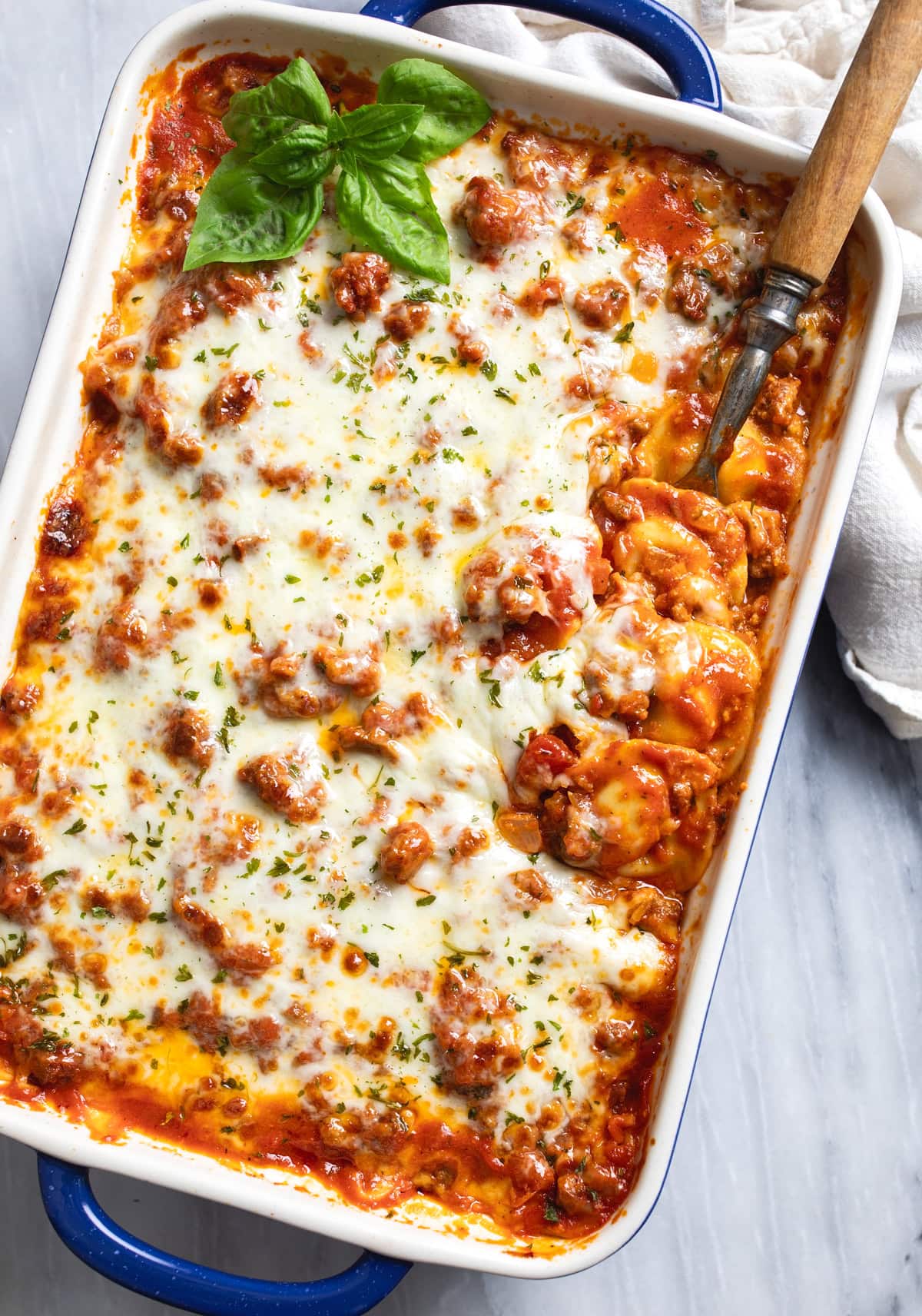 Ravioli Lasagna in a casserole dish with a serving spoon on the side and fresh basil on the side.
