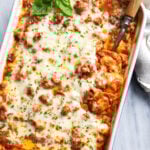 Ravioli Lasagna in a white casserole dish with fresh basil on top and a serving spoon on the side.
