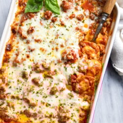 Ravioli Lasagna in a white casserole dish with fresh basil on top and a serving spoon on the side.