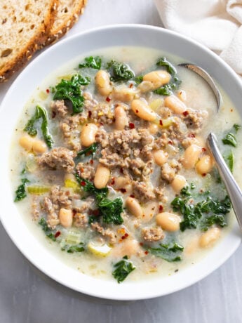 Sausage and White Bean Soup with kale in a white bowl with a spoon on the side.
