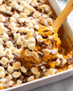 A wooden spoon scooping Sweet Potato Casserole from a white casserole dish.