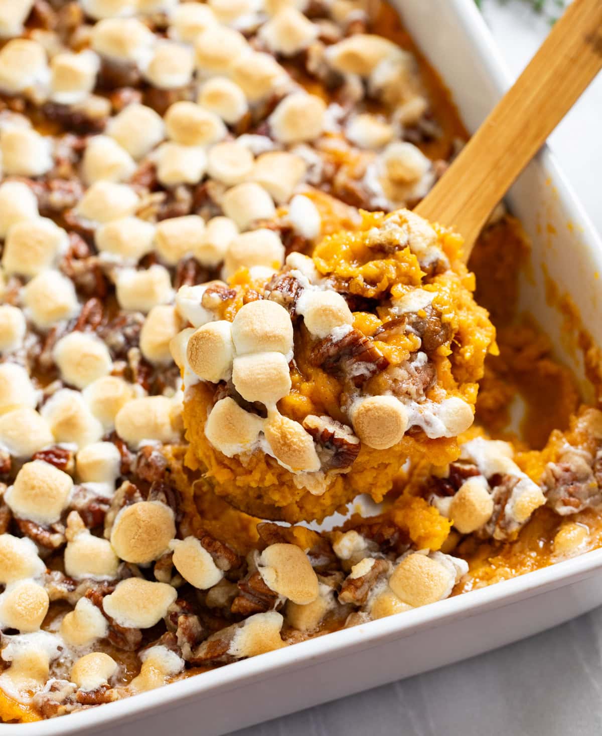 A wooden spoon scooping Sweet Potato Casserole from a white casserole dish.